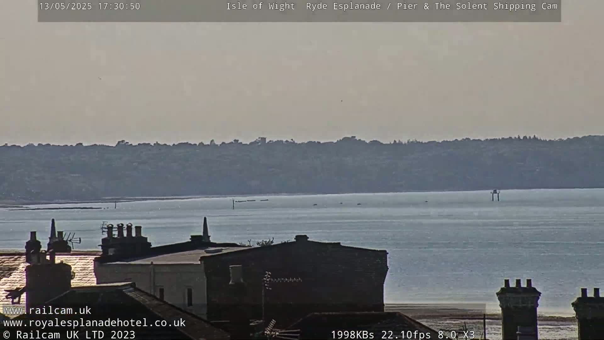 A hazy, calm day overlooks a body of water with a distant shoreline and rooftops in the foreground.