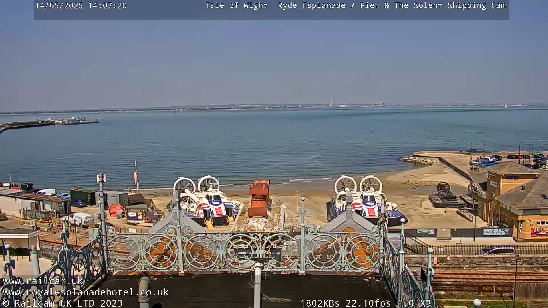 Two hovercrafts are parked on a sandy beach near a body of water on a sunny day.