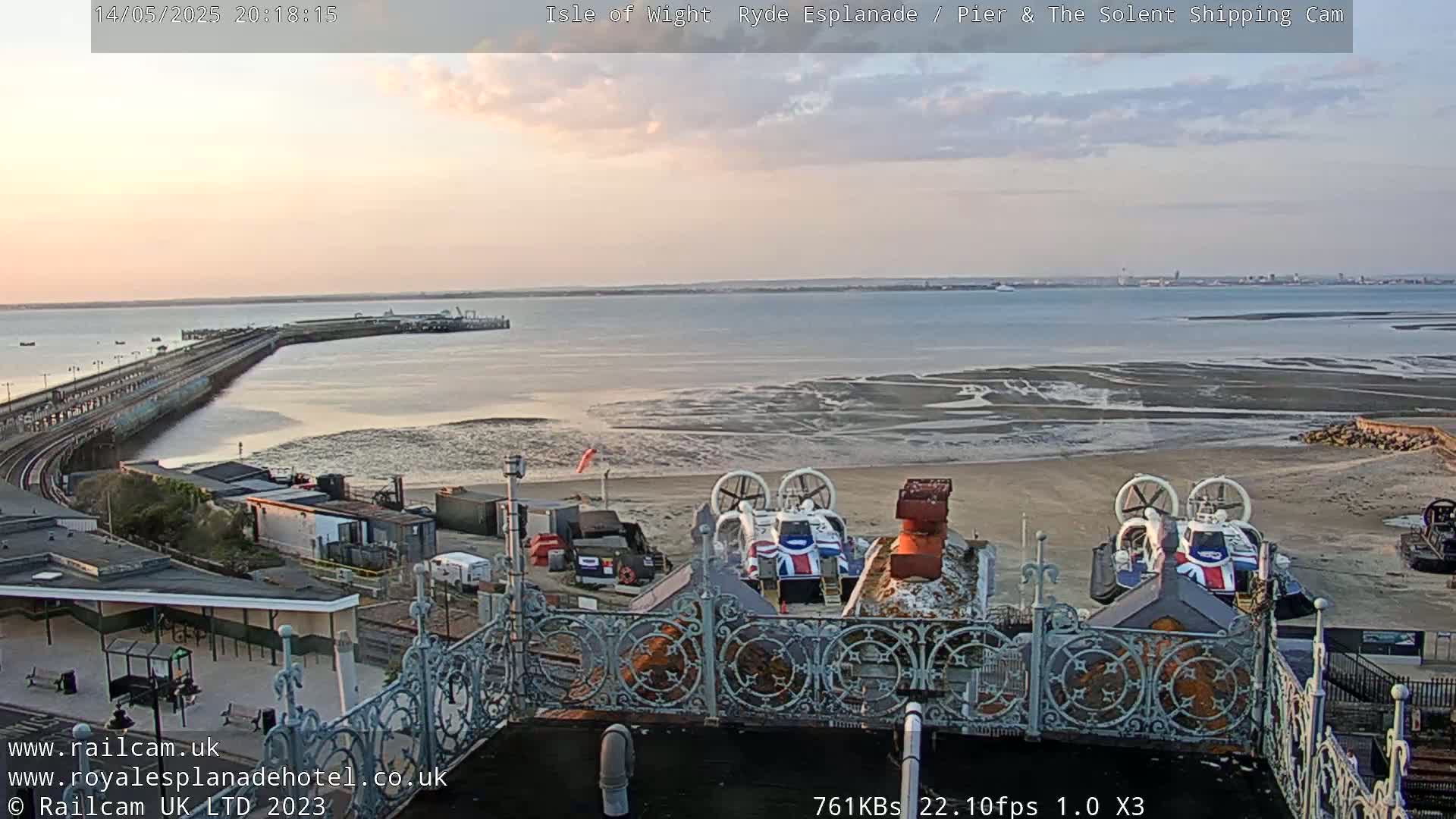 Two hovercrafts are parked on a beach near a pier and body of water at sunset.