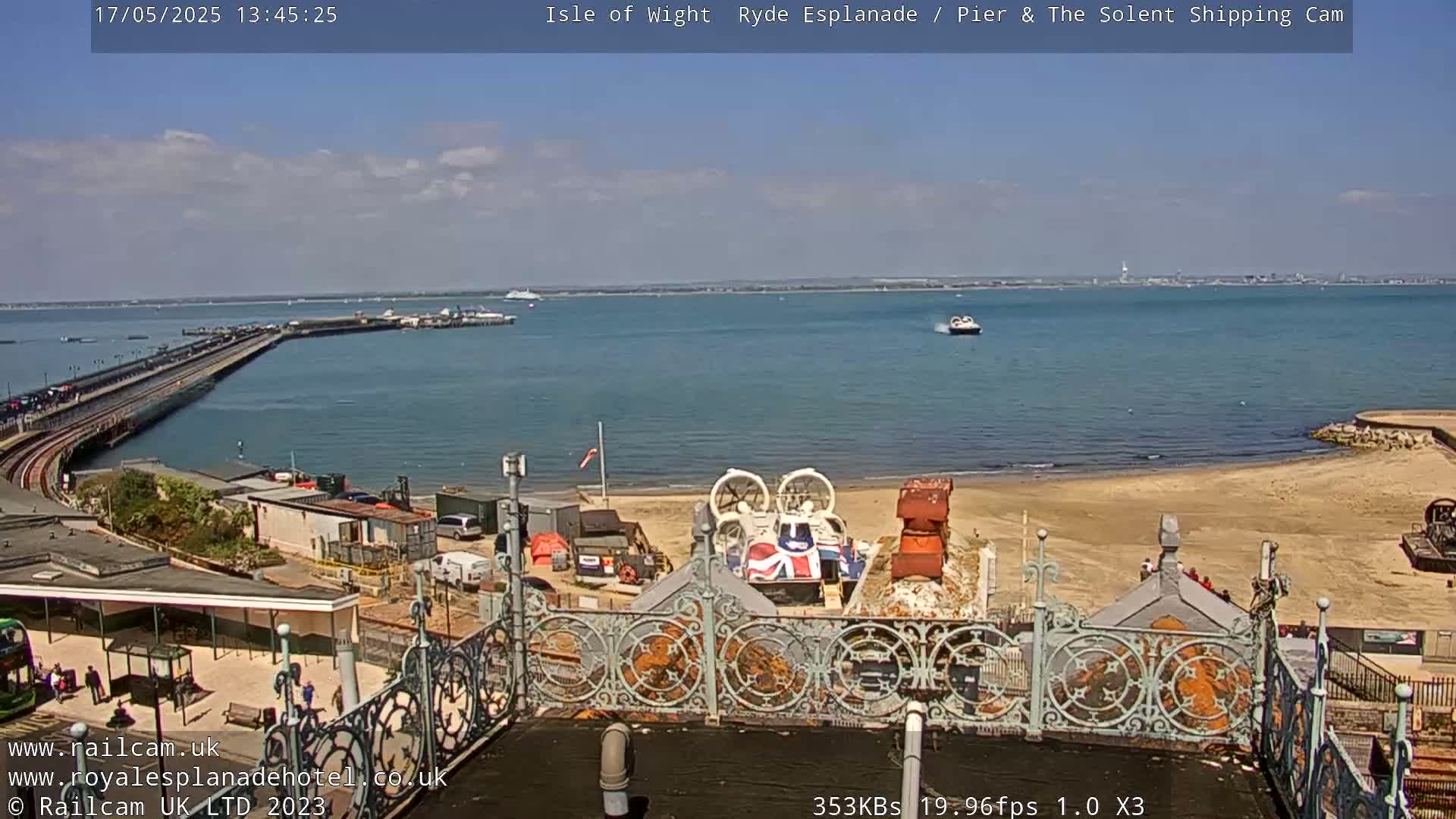 A hovercraft sits on a sandy beach near a pier and body of water under a partly cloudy sky.