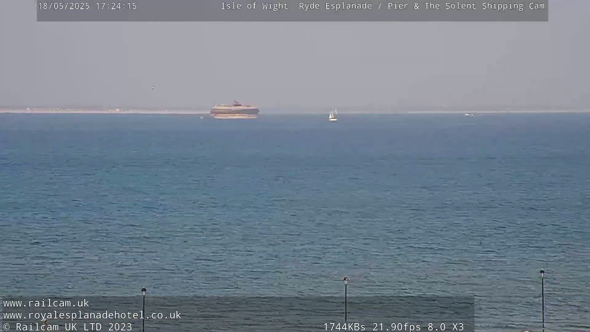 A large body of calm water shows a distant ferry and sailboat on a hazy day.