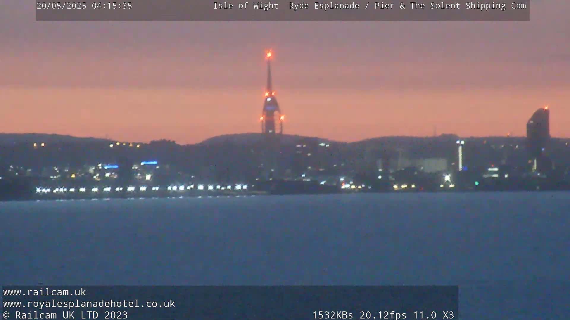 A city skyline at dusk is seen across a calm body of water, with a tall tower lit up in the center.