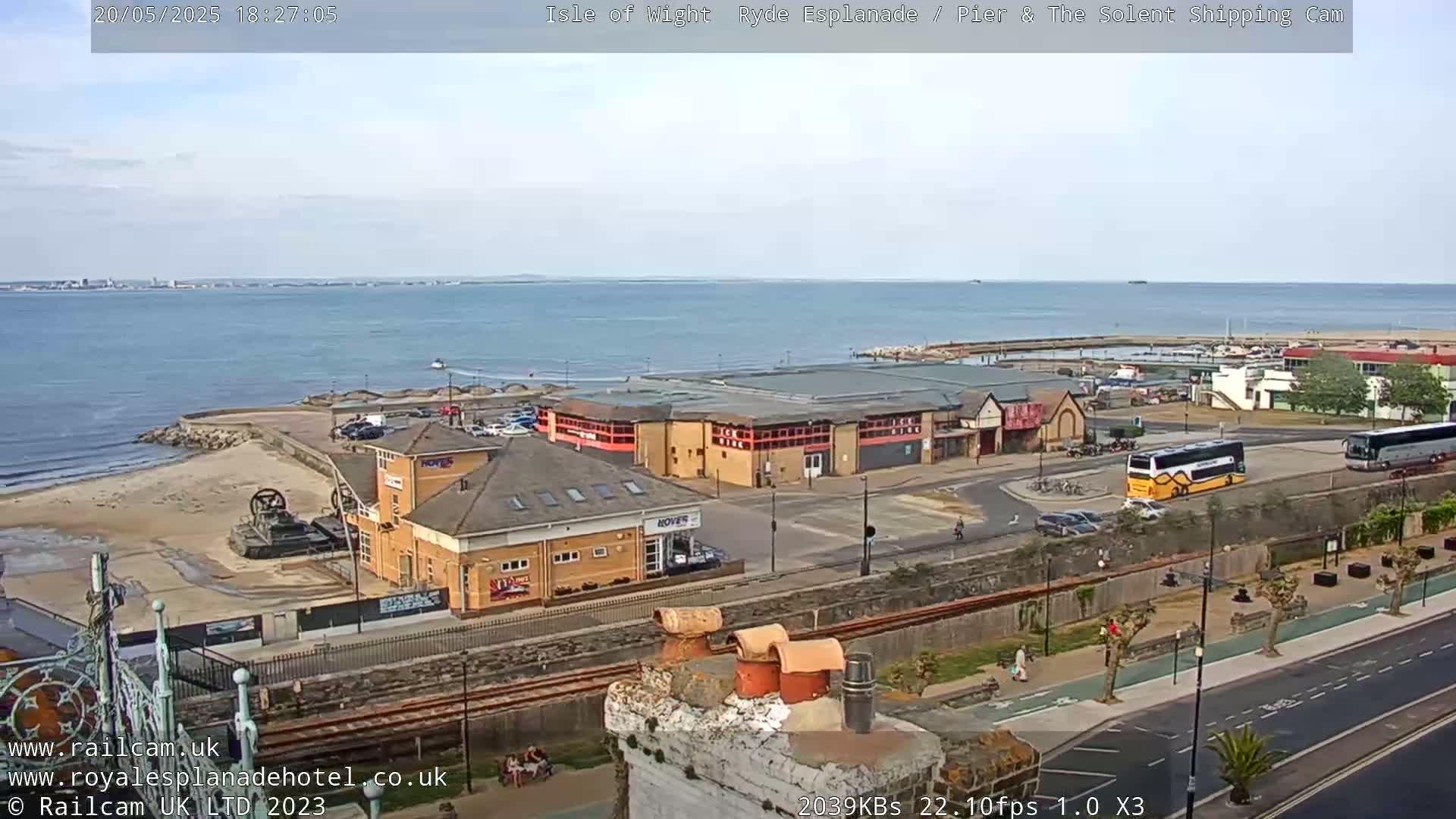 A seaside town with buildings, vehicles, and a beach is visible under a partly cloudy sky.