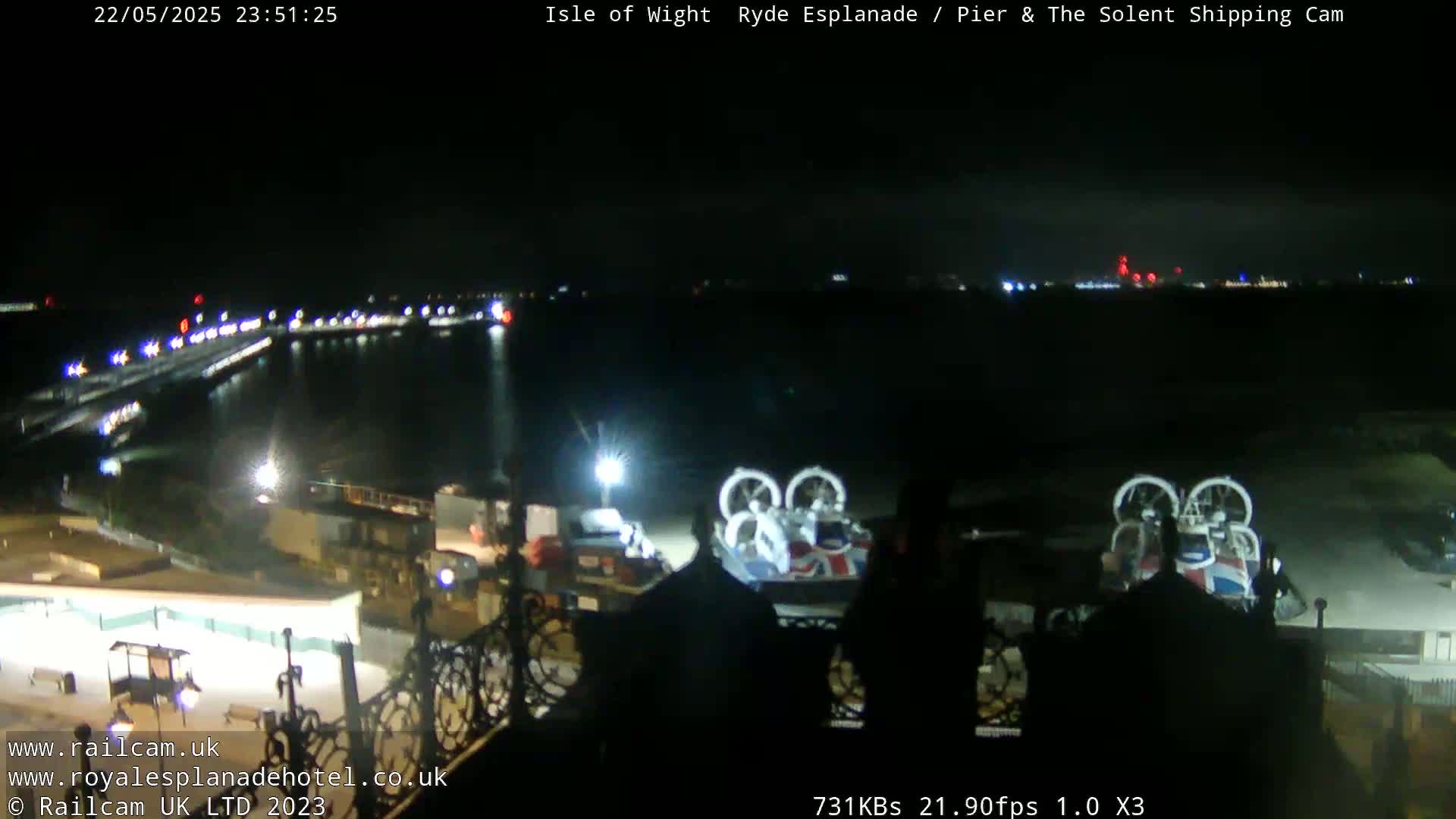 A nighttime view of a harbor with two hovercrafts docked, illuminated by lights on the pier and across the water.