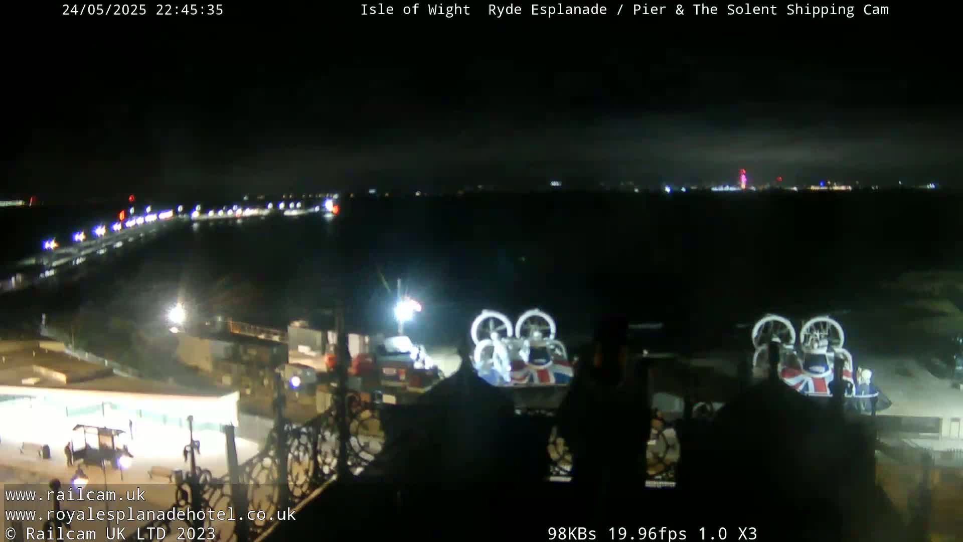A nighttime view of a waterfront area with several hovercrafts docked near a pier, under a dark, clear sky.
