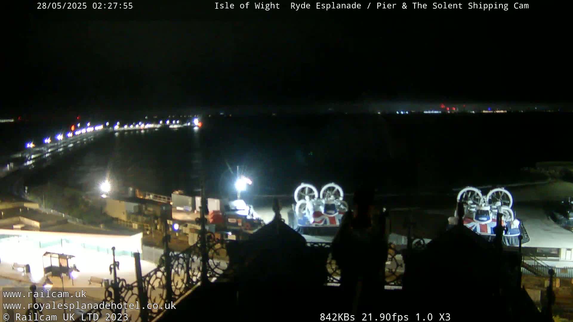 A nighttime view of a waterfront area with two hovercrafts and a shoreline illuminated with lights.