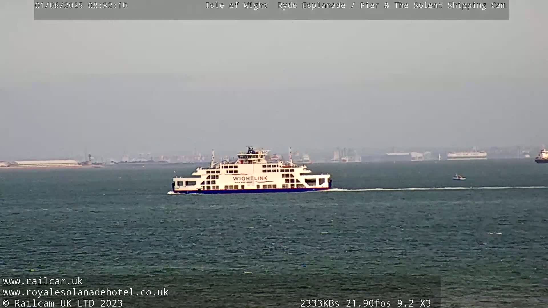 A large ferry sails on a calm, hazy body of water, with a distant shoreline visible on the horizon.