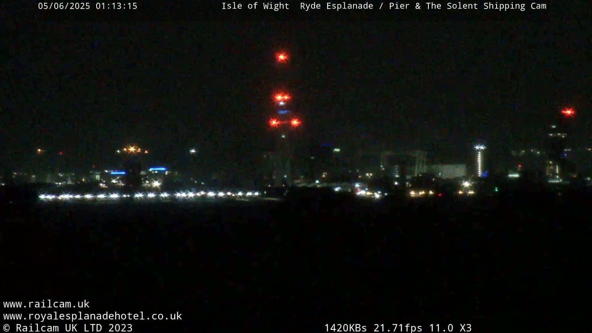 A nighttime view of a city skyline illuminated by various lights, including a tall structure with red lights near the top.