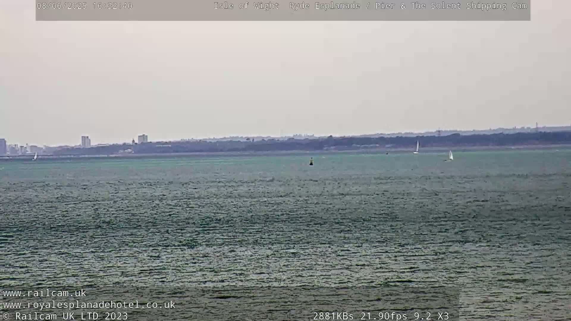 A calm, overcast day shows a wide expanse of greenish-grey water with a few sailboats and a distant shoreline.
