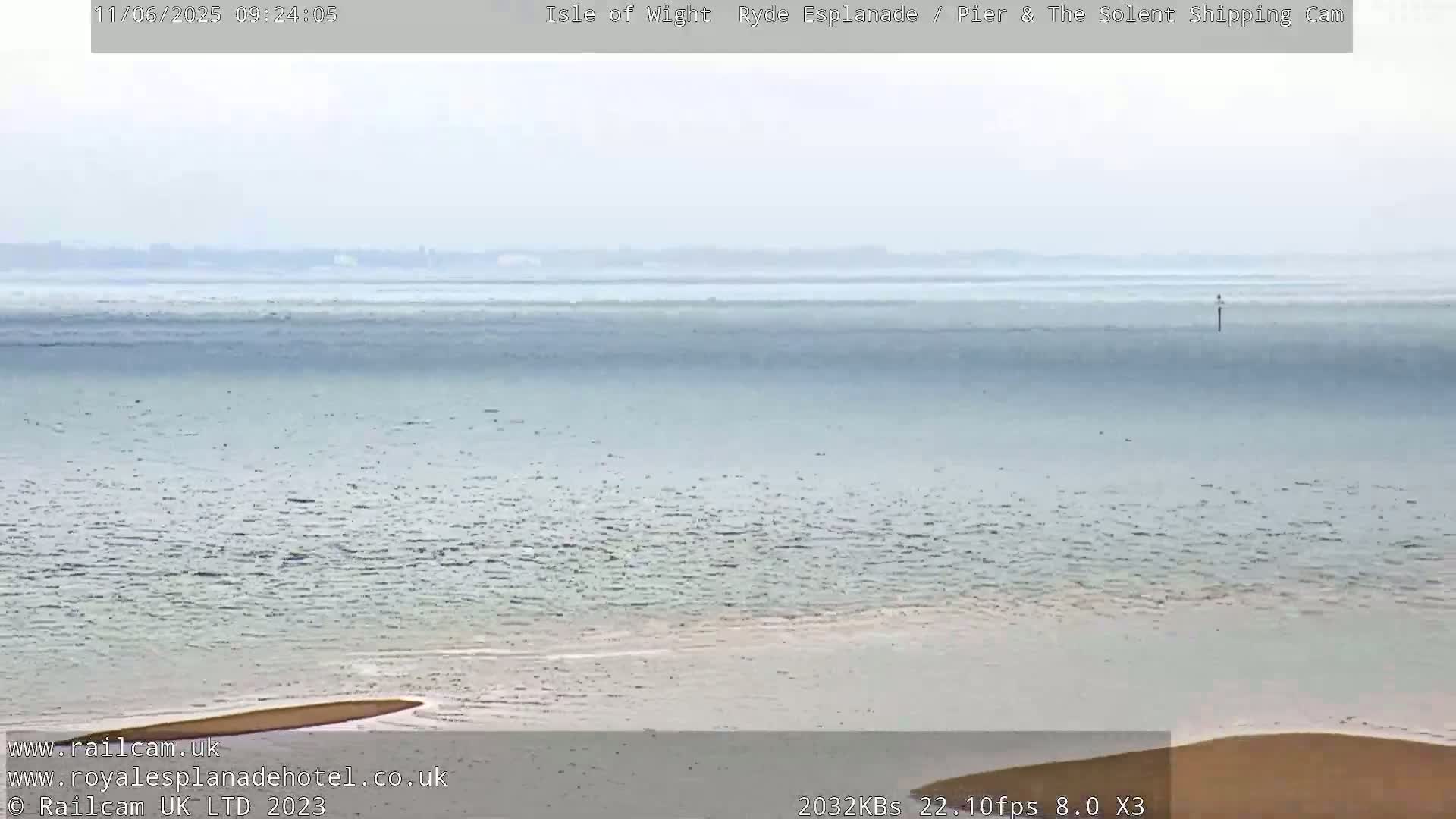 A hazy, calm body of water stretches to a distant shoreline under an overcast sky.