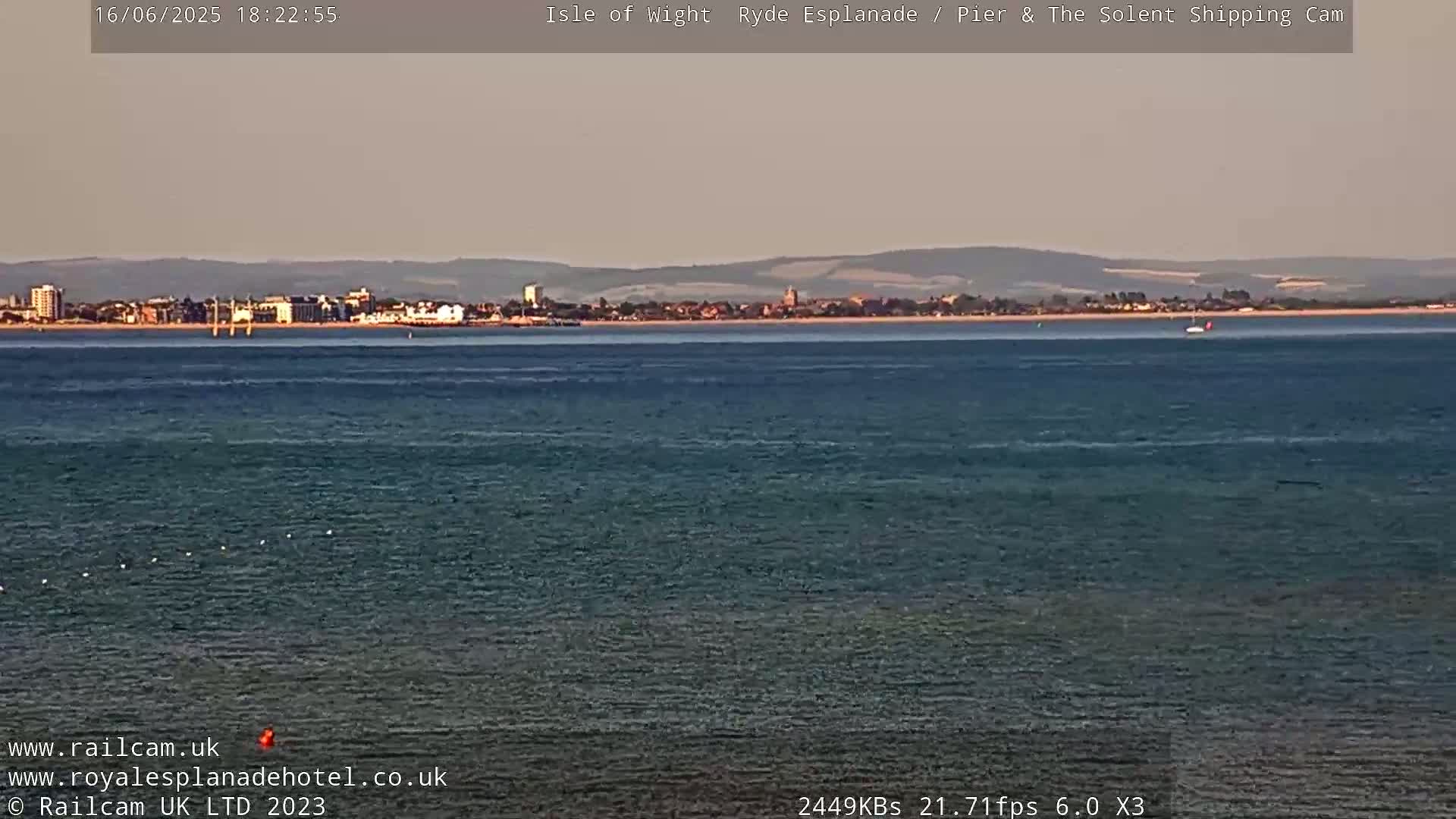 A calm body of water shows a distant town under a hazy, light-colored sky.