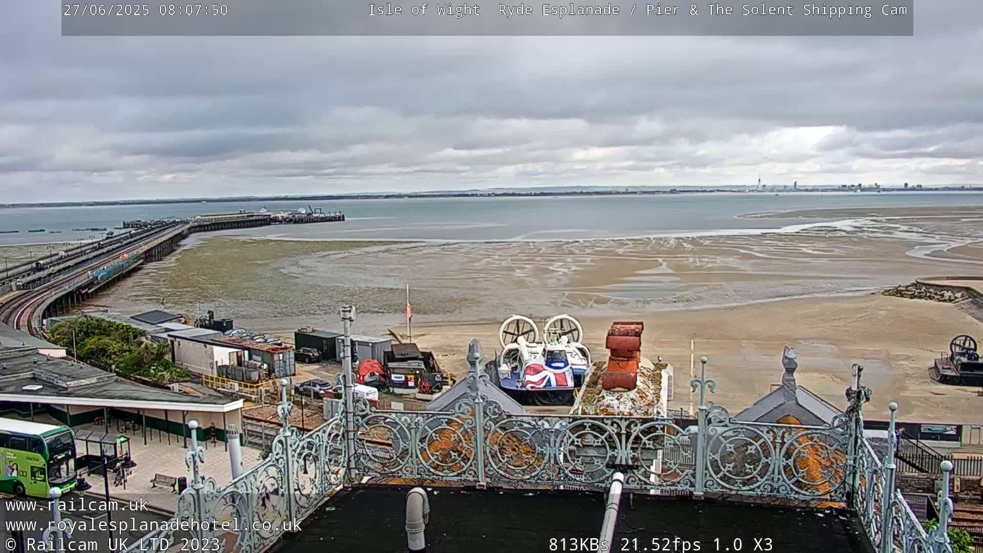 A hovercraft sits near a pier and expansive shoreline with low tide under a cloudy sky.