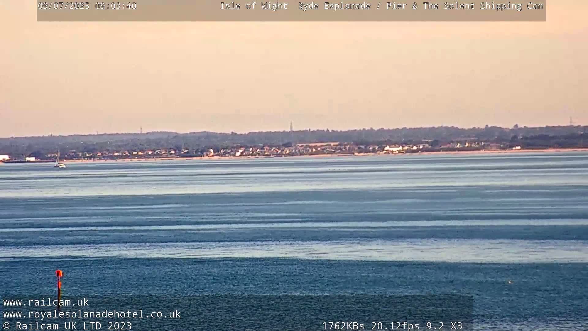 A calm body of water stretches to a distant shoreline under a pale sky.
