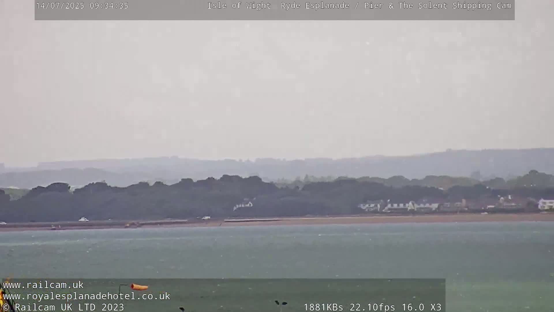 A hazy, overcast day shows a calm body of water with a distant shoreline featuring dark green vegetation and a few buildings.