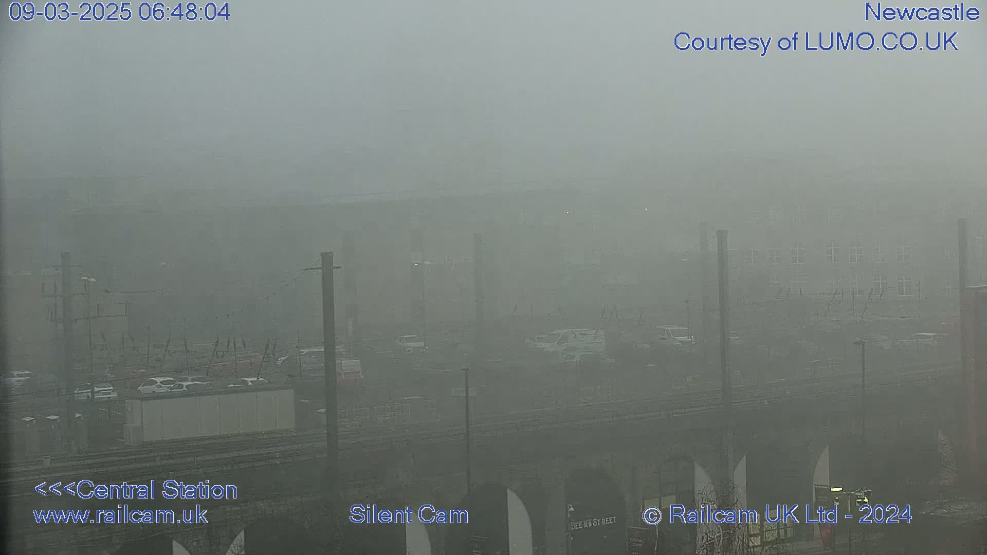 A foggy view of a cityscape shows a train station and railway lines below, partially obscured by dense fog.