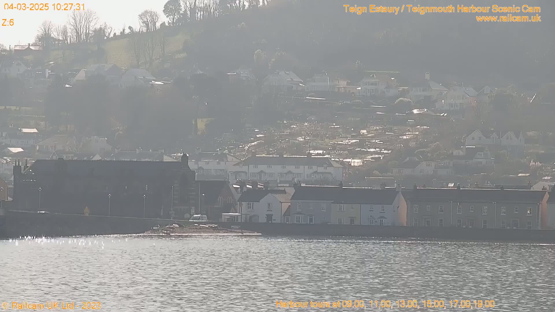A hazy view of a town situated on a hillside overlooking a calm body of water.