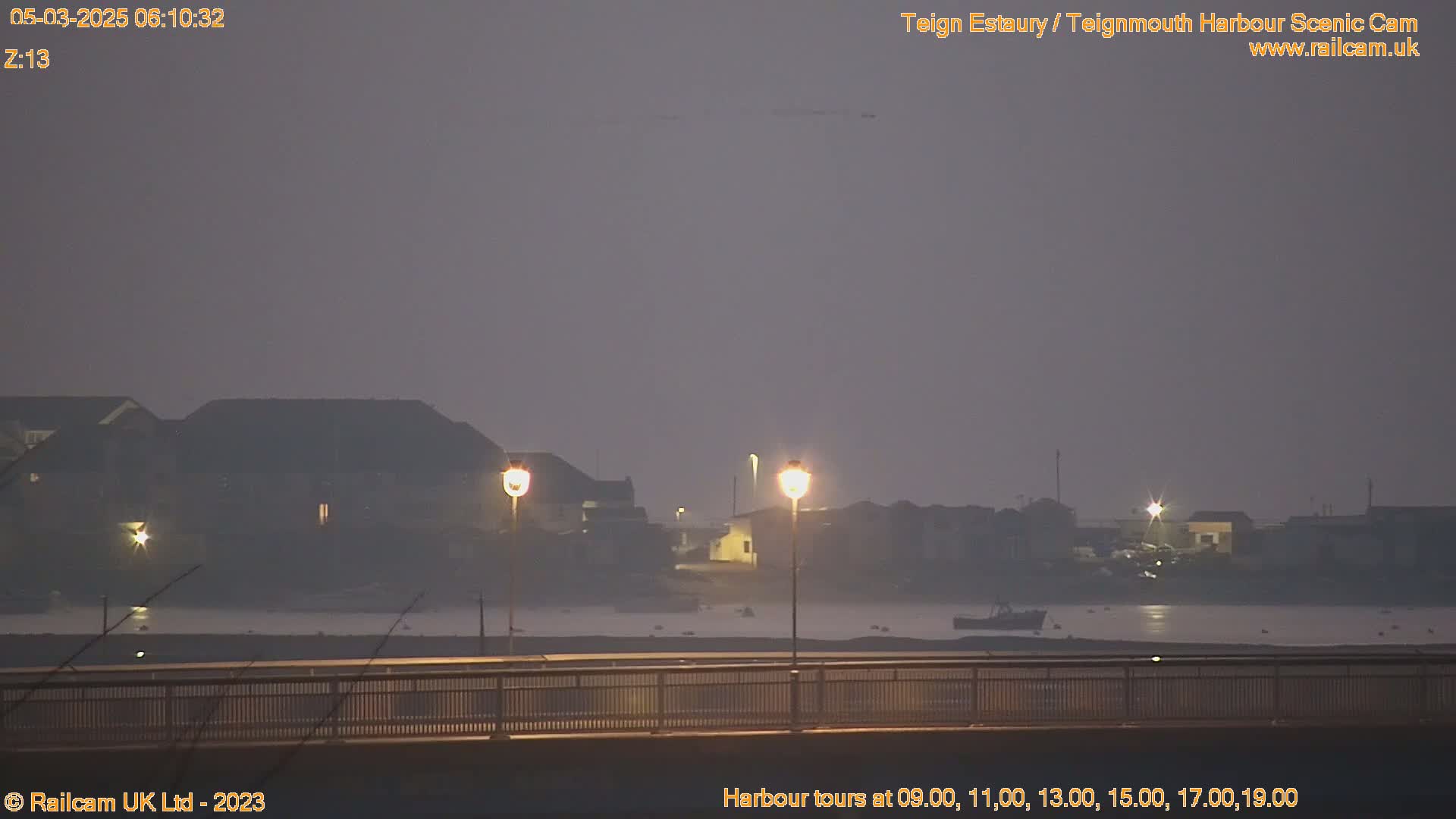 A hazy, dimly lit harbor scene at dawn is viewed from a bridge, with buildings and boats visible in the distance.