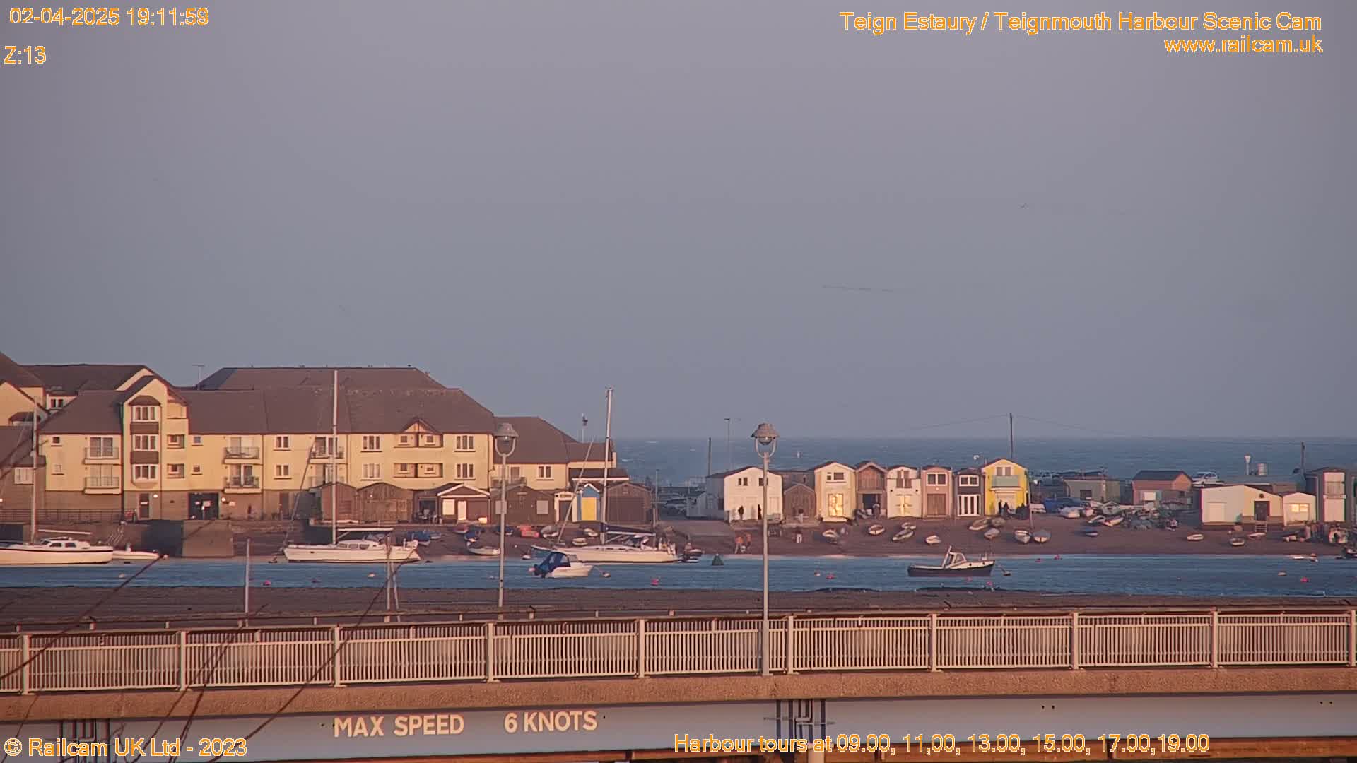 A seaside town with buildings and boats is visible under a dusky sky at twilight.