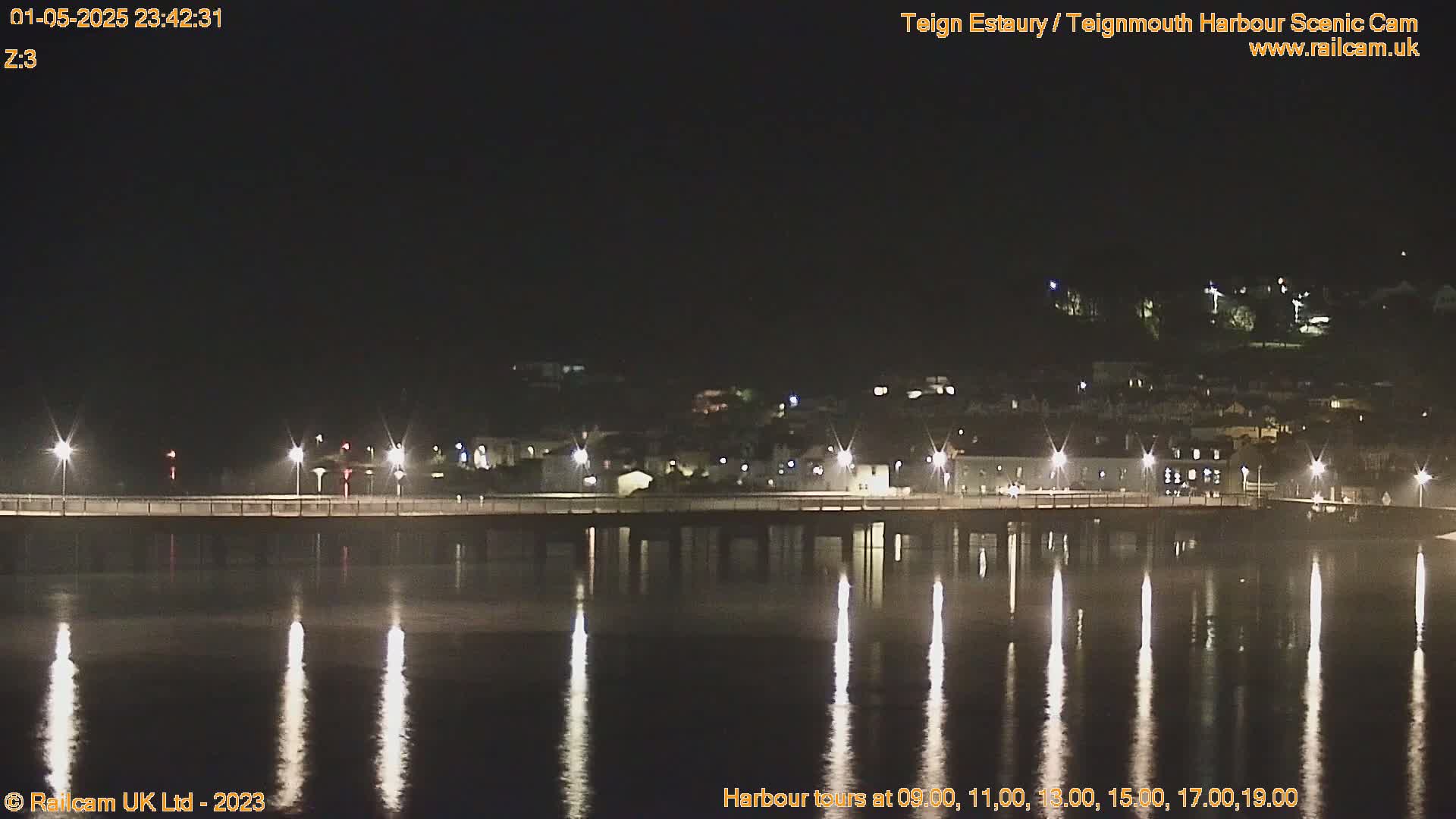 A long pier with lights stretches across a calm body of water reflecting the lights at night.