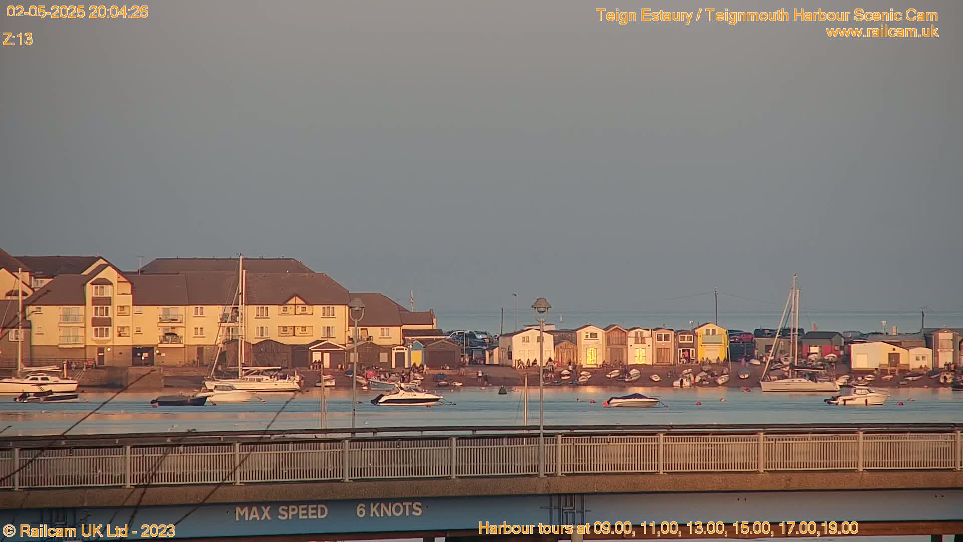 A calm, dusky evening scene shows a harbor with boats, buildings, and a bridge, under a pale sky.