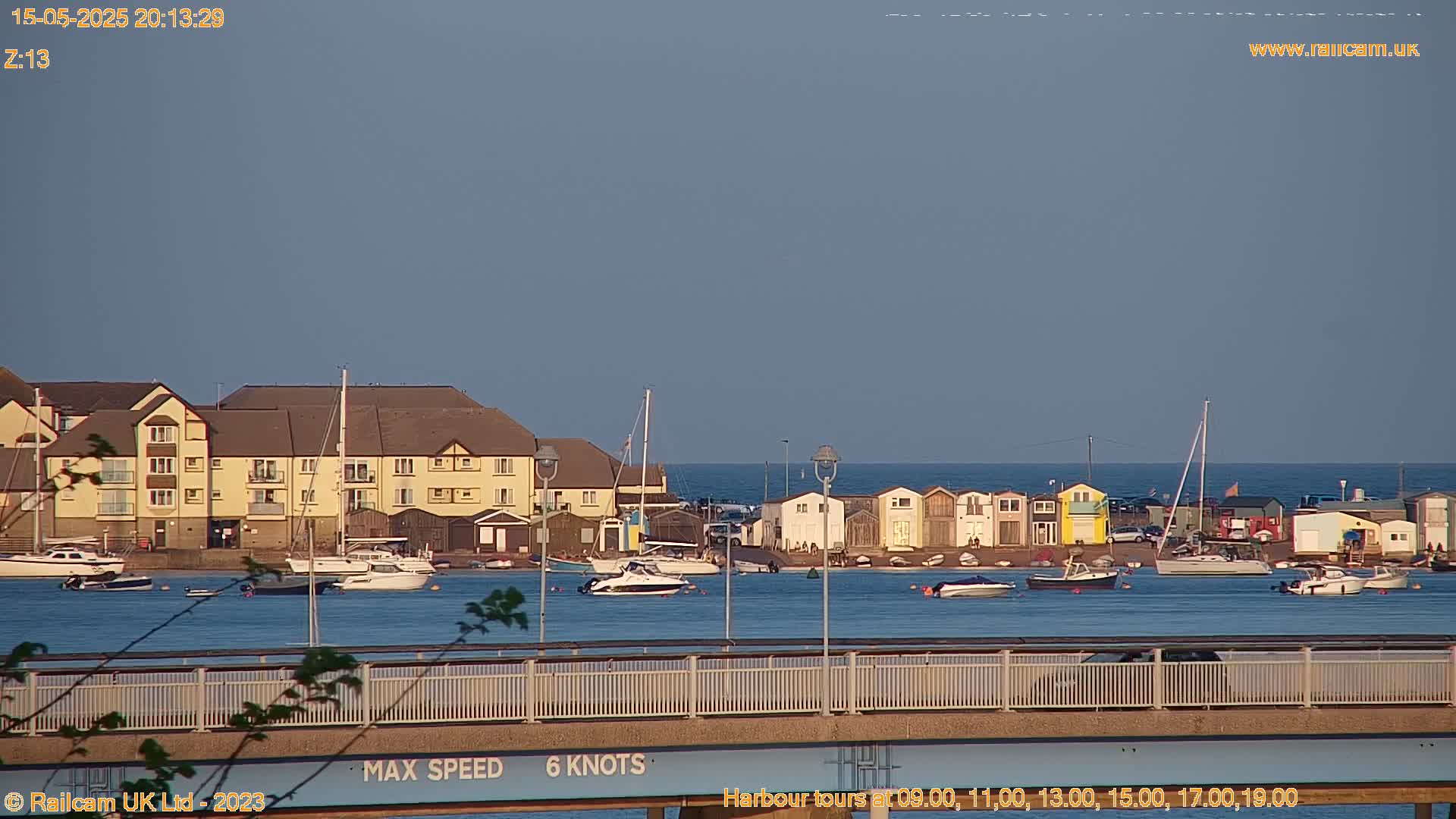 A calm body of water with numerous boats and a waterfront building is seen under a clear, twilight sky.