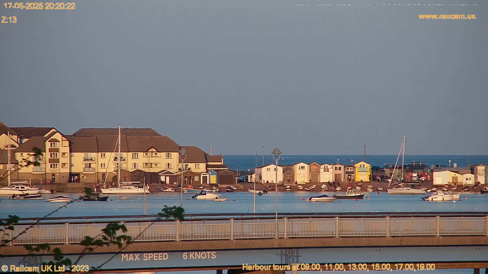 A calm, twilight scene shows a harbor with boats, buildings, and a bridge in the foreground.