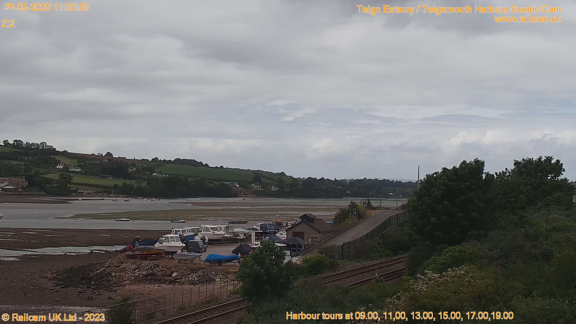 A wide shot of a harbor with several small boats docked on a mostly muddy shore under an overcast sky.