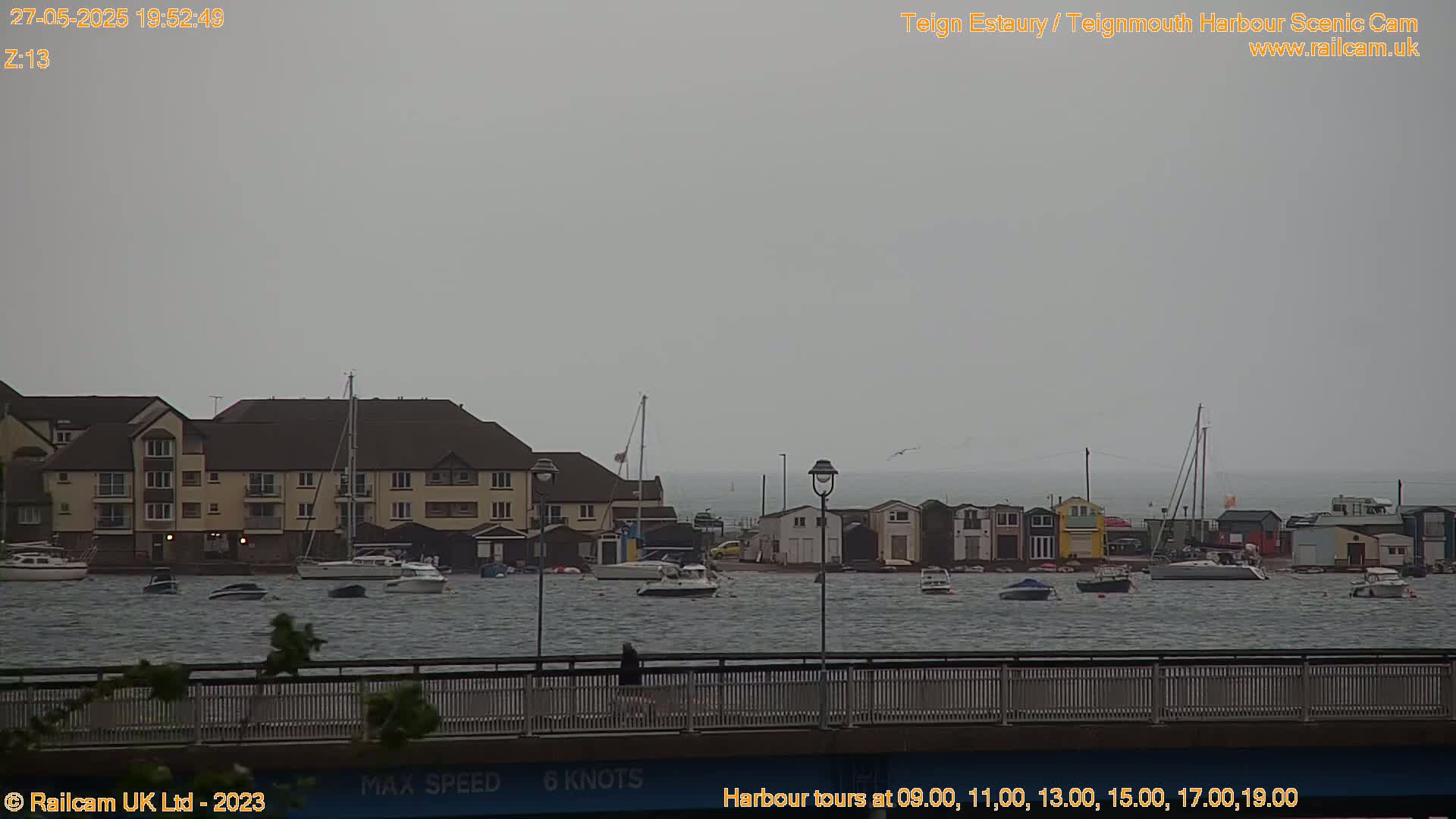 A harbor scene on an overcast day shows several boats in choppy water near a multi-story building and colorful smaller structures.