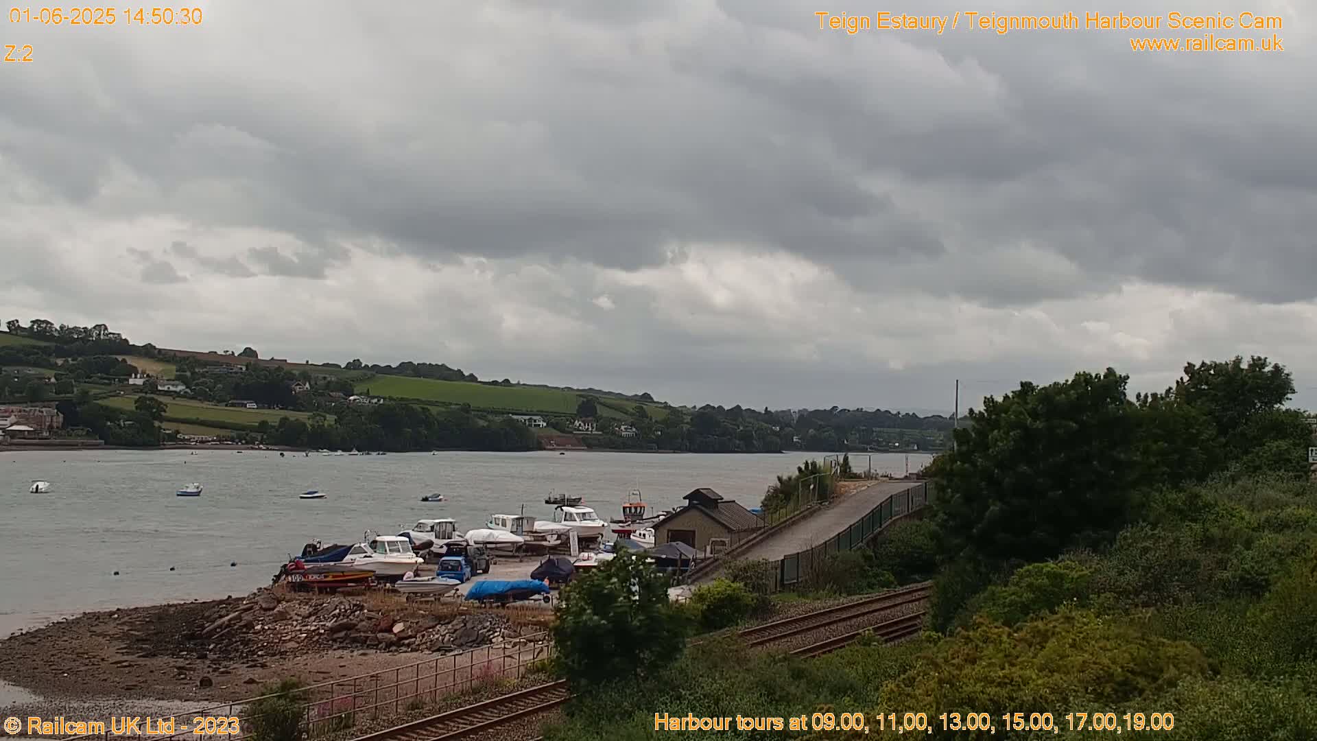 A harbor with numerous boats docked near a shoreline under an overcast sky.