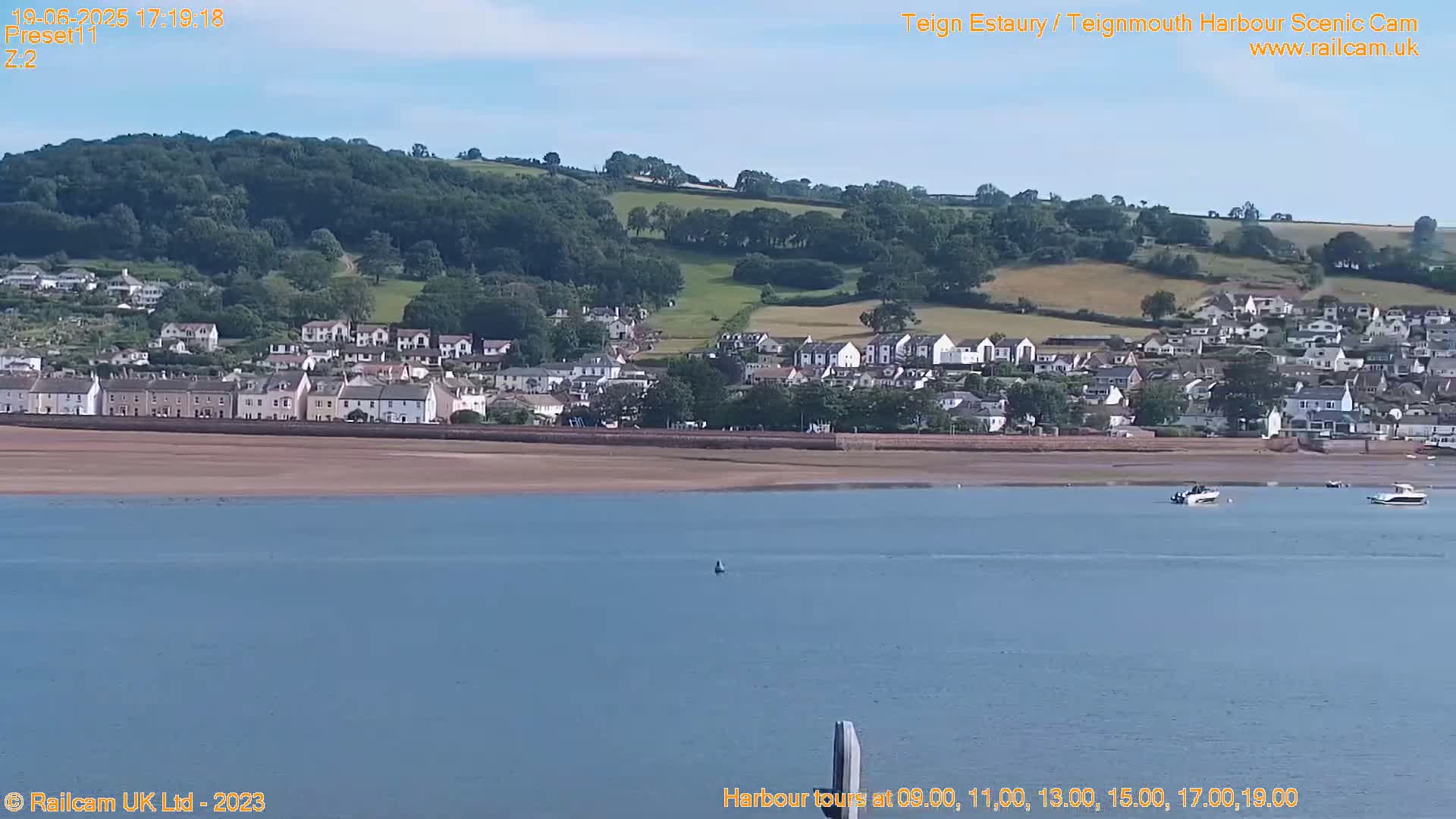 A coastal town sits on a sandy shore next to a calm body of water under a clear sky.