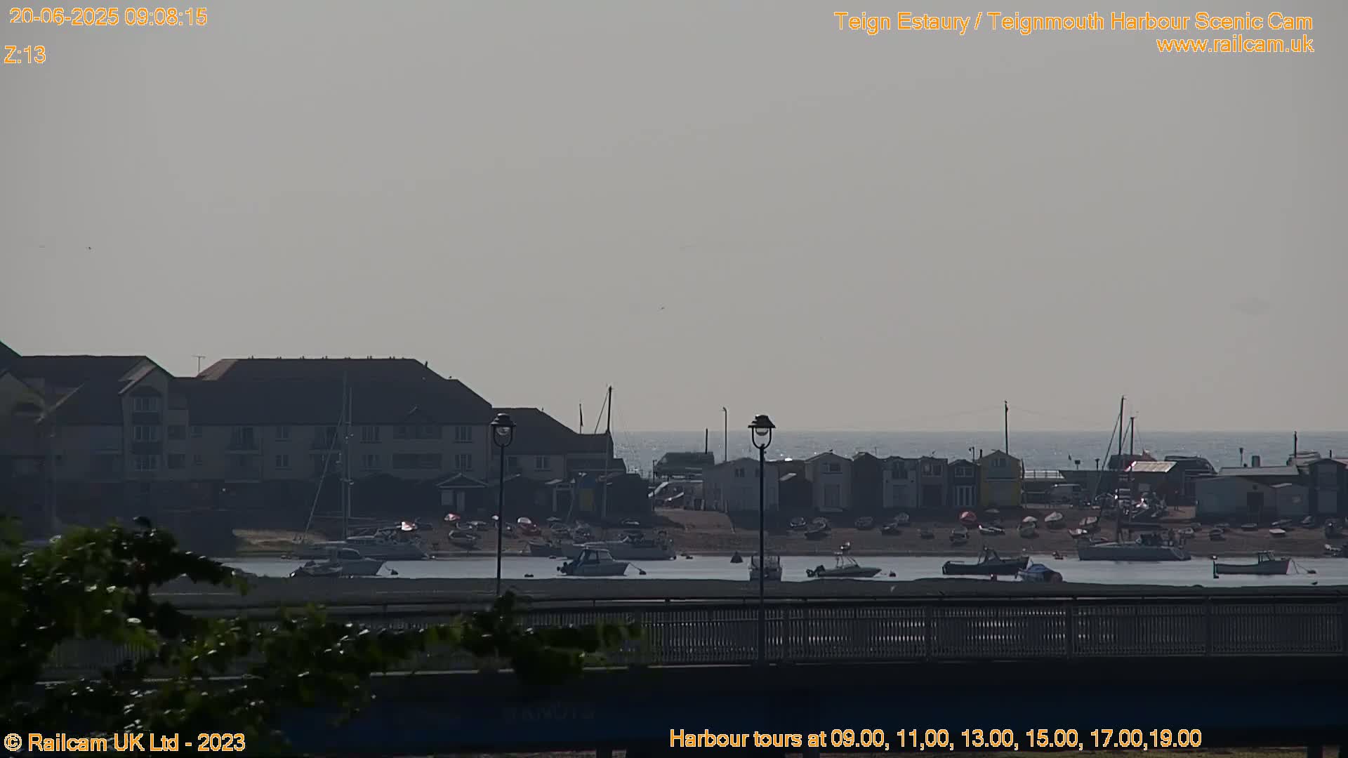 A hazy day reveals a harbor scene with several boats, buildings, and a low-lying bridge in the foreground.
