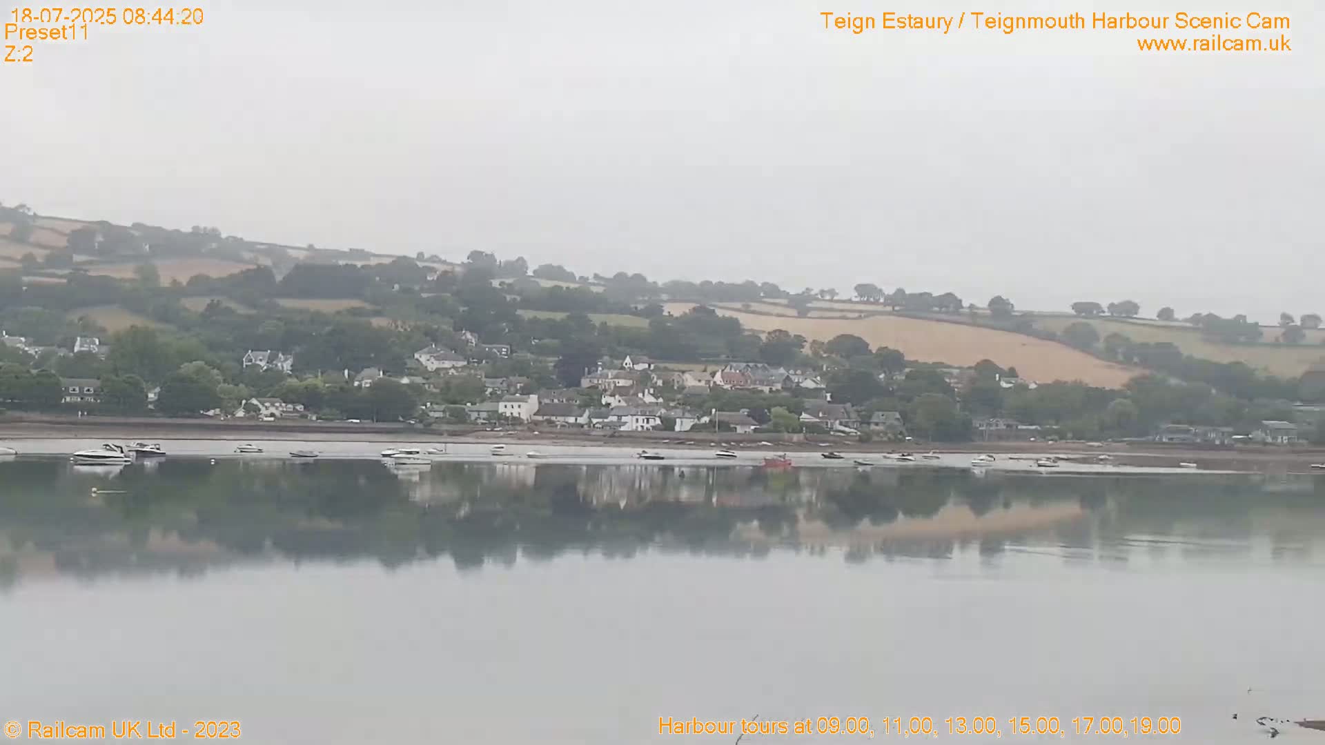 A calm body of water reflects a hazy, overcast sky and a small town nestled along a hillside.
