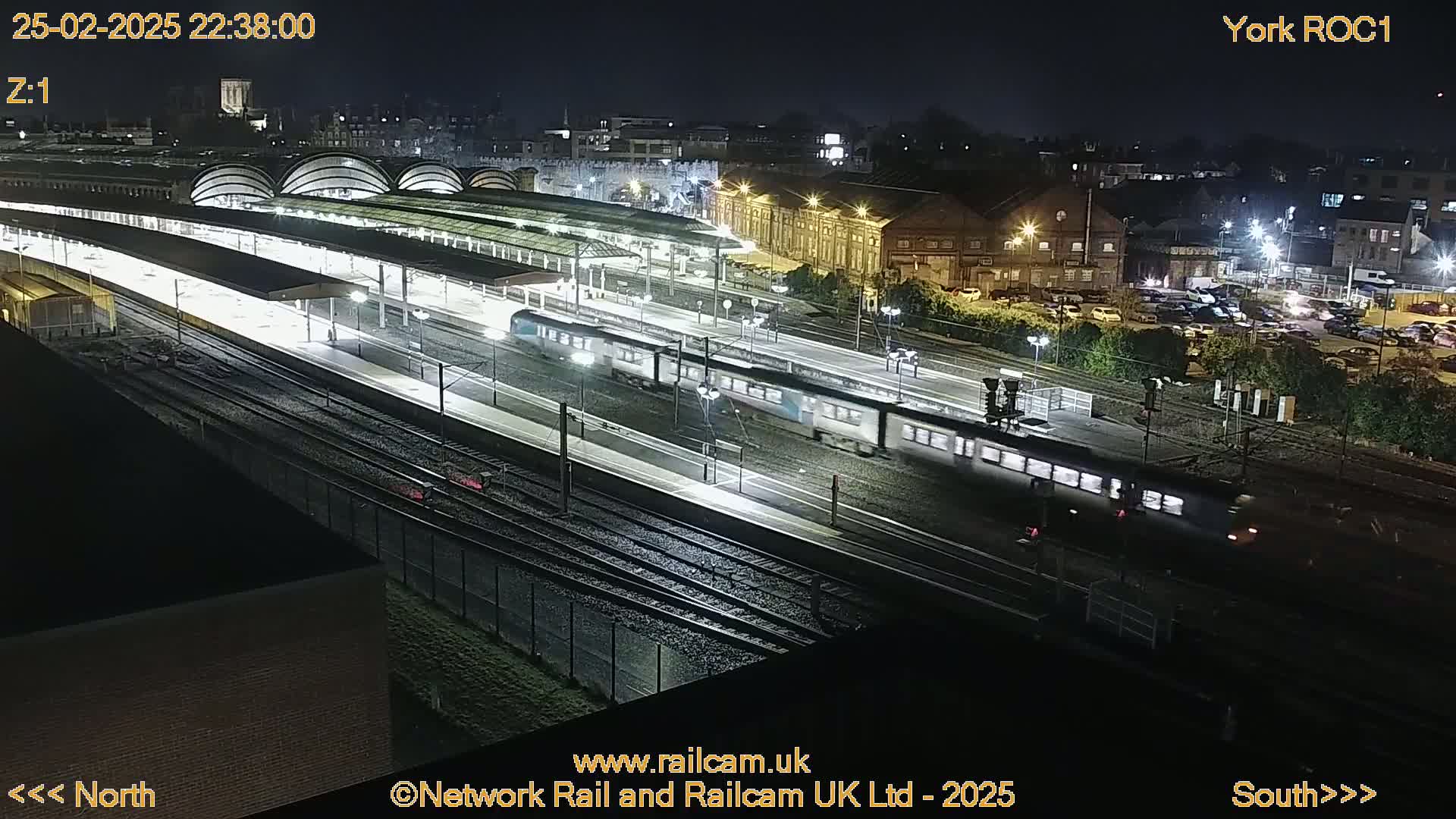 At night, two trains pass through a brightly lit train station with many tracks.
