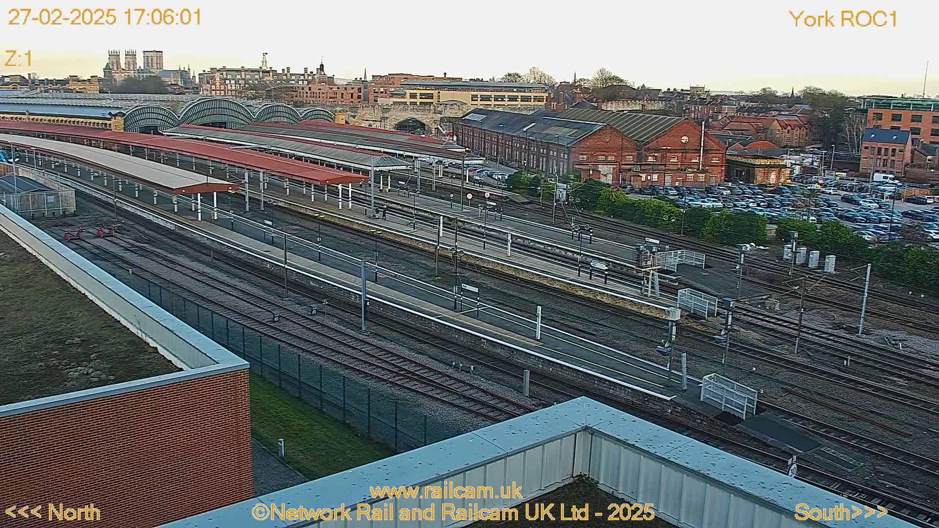 A high-angle view of a train station with numerous tracks and platforms under a partly cloudy sky.
