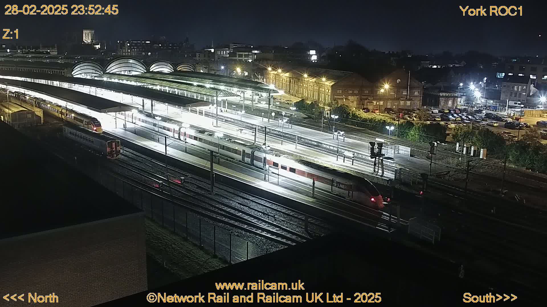 A nighttime, overhead view of a brightly lit train station with multiple trains on tracks.