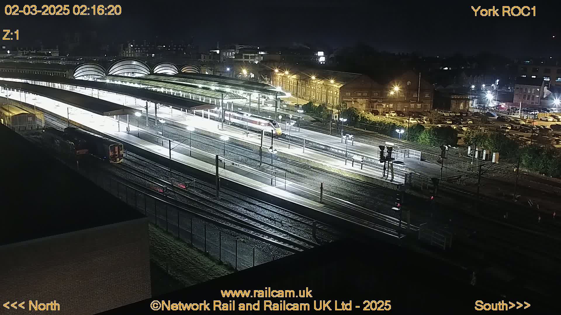 A brightly lit train station at night with two trains on the tracks.