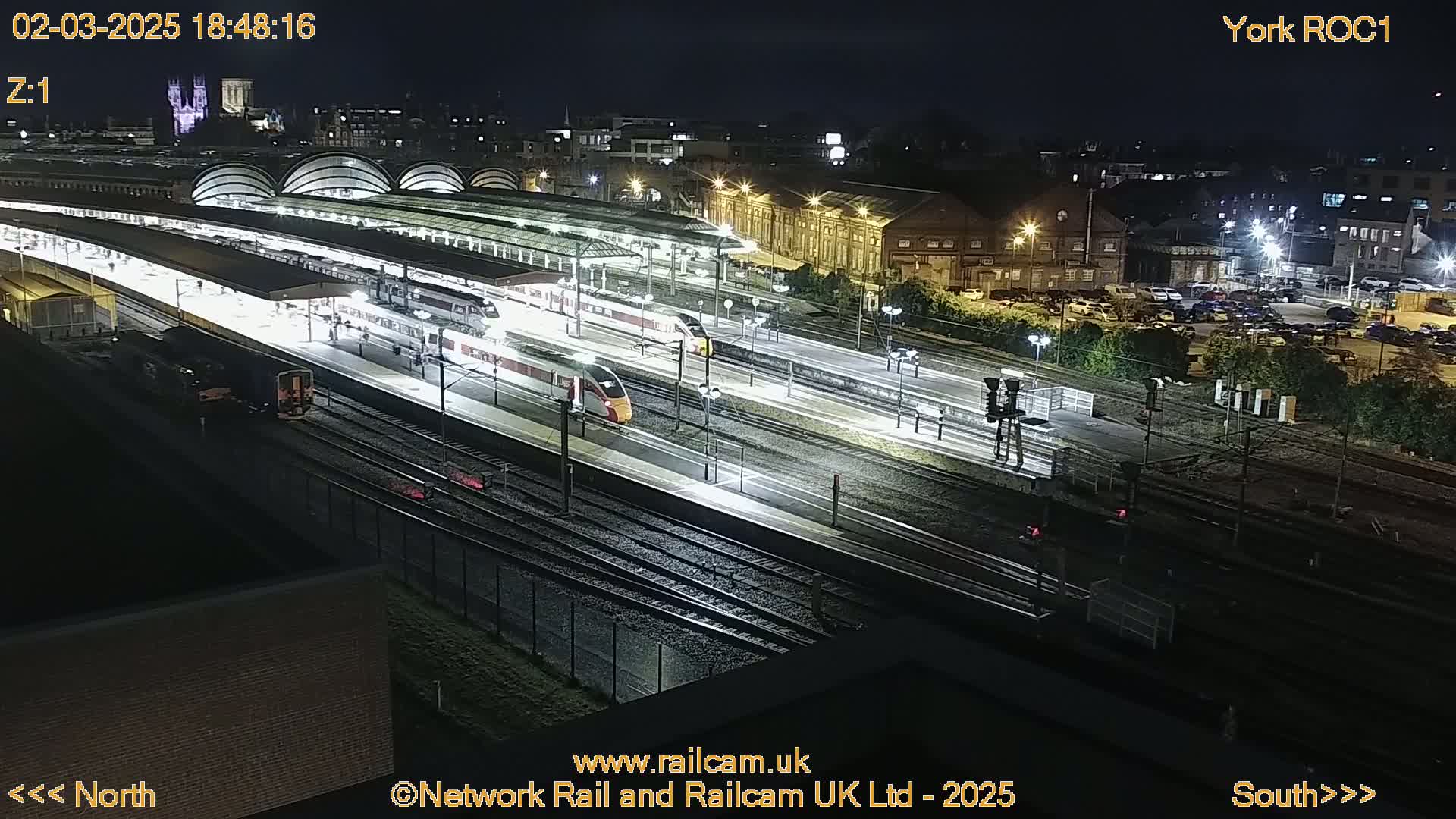 A nighttime, high-angle view of a train station with several trains at platforms and tracks, illuminated by artificial lights.