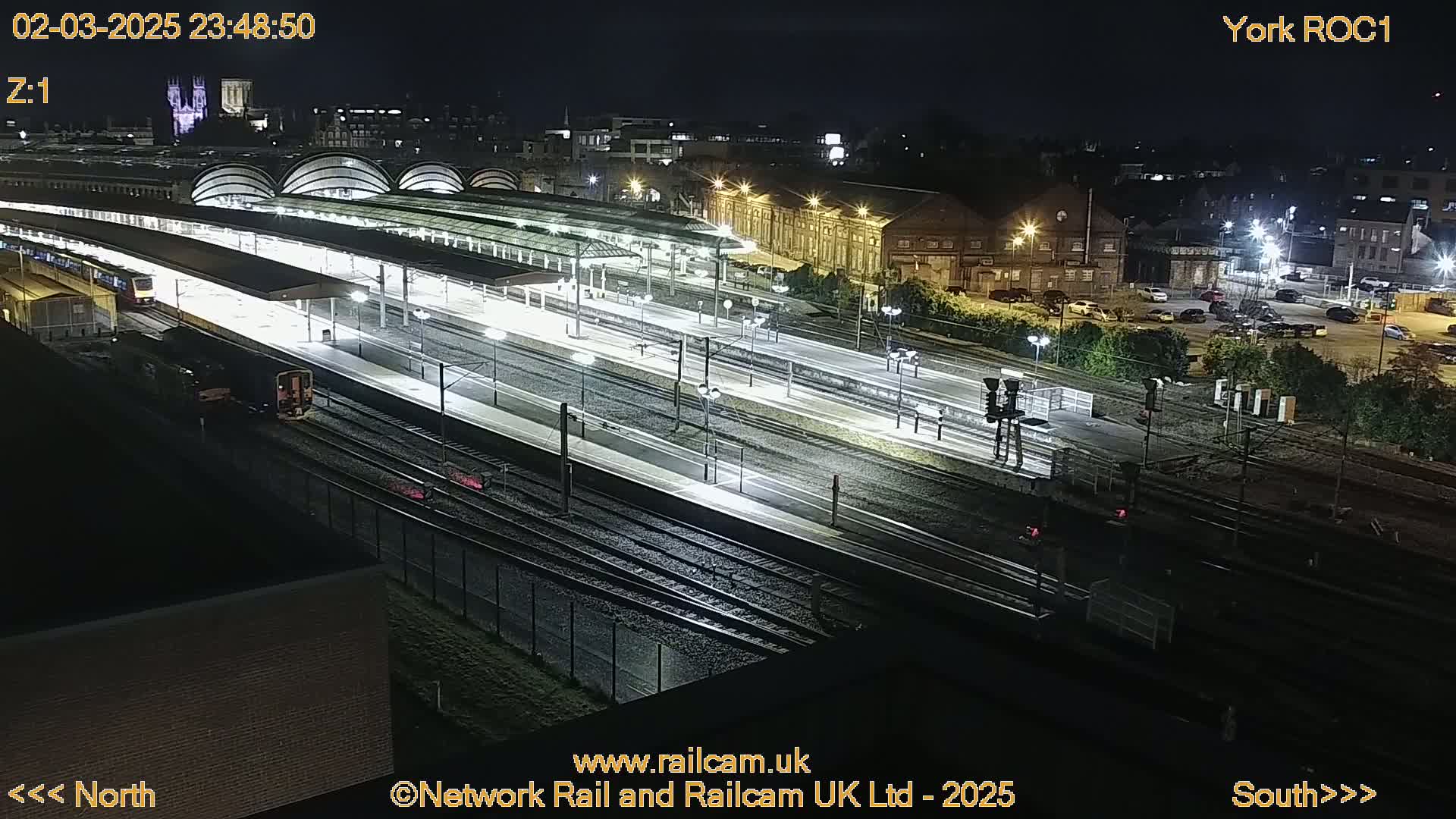 A nighttime aerial view of a brightly lit train station with several trains on the tracks.