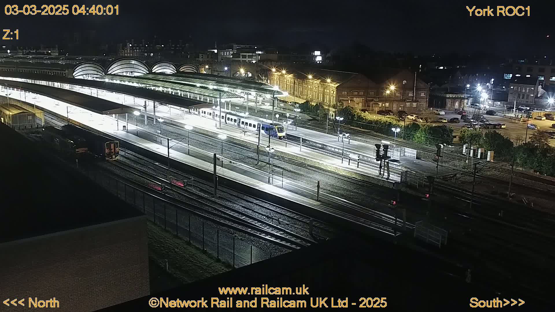 A nighttime, high-angle view of a brightly lit train station with several trains on the tracks.