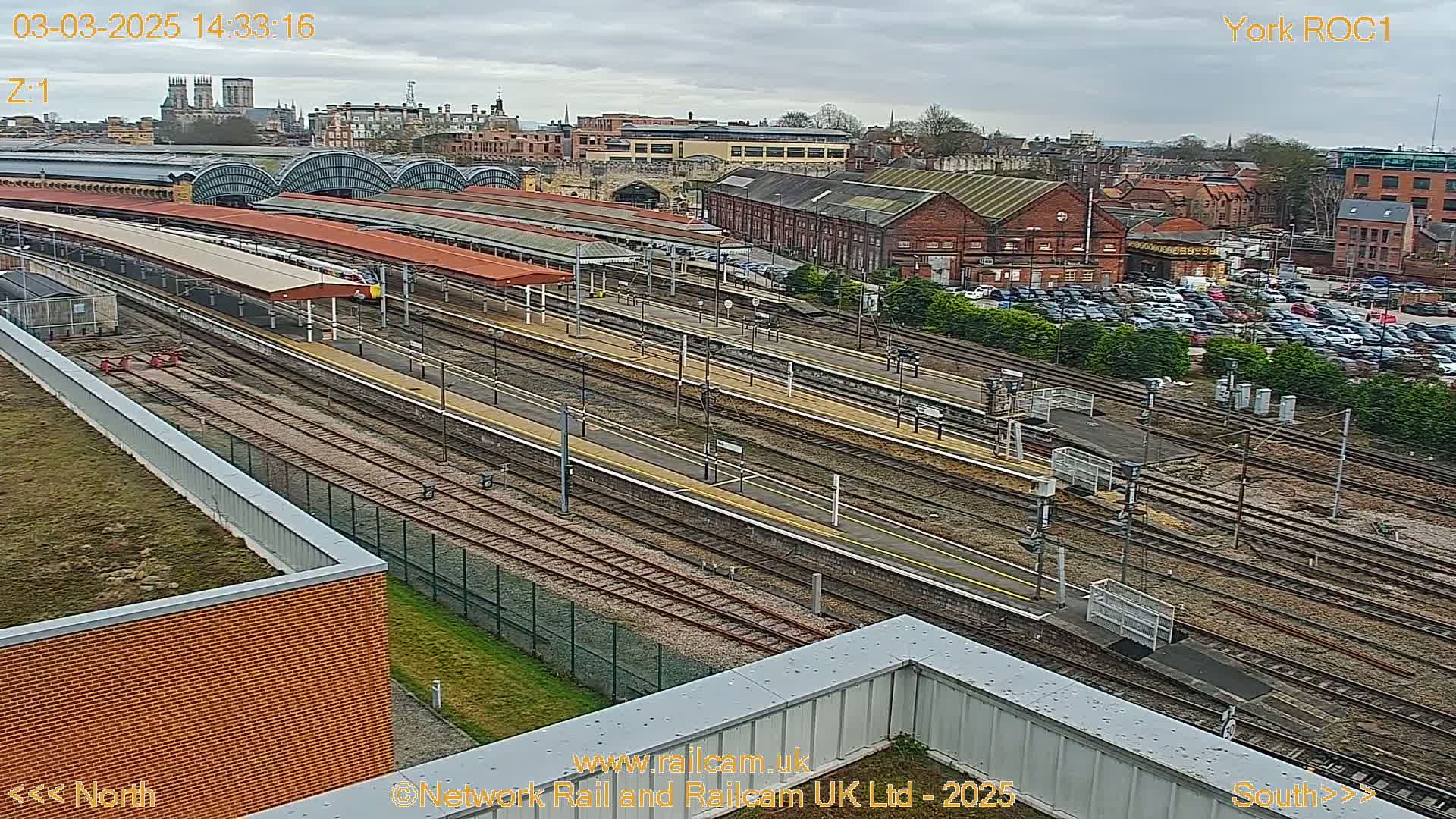 A high-angle view of a train station with numerous tracks and platforms under an overcast sky.
