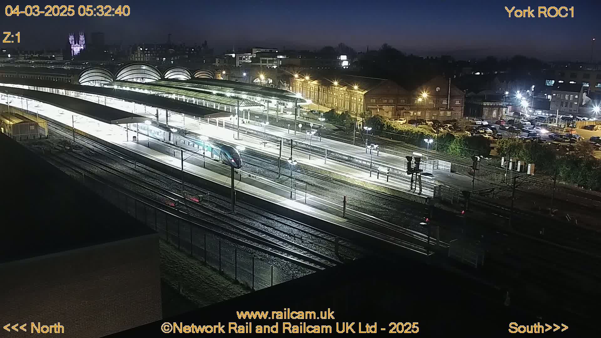 A nighttime, high-angle view of a train station with a train on the platform, illuminated by artificial lights.