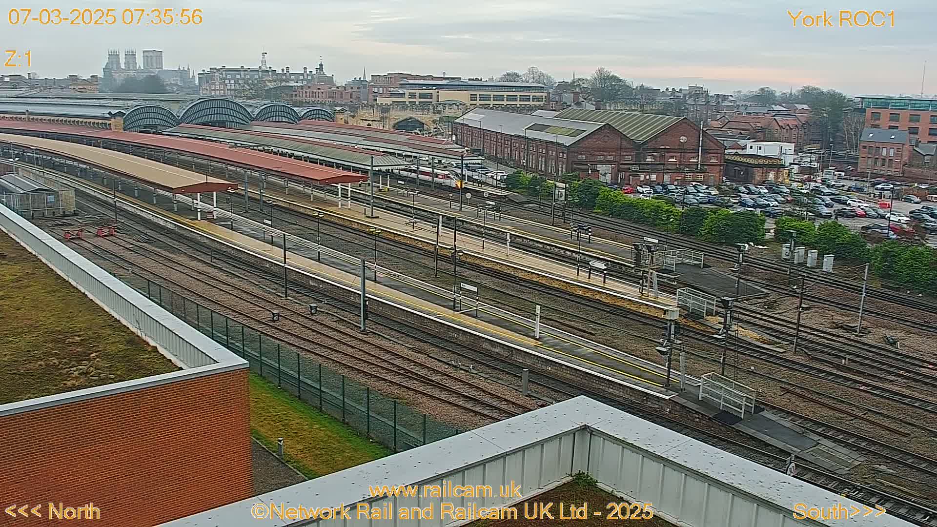 A high-angle view of a train station with numerous tracks and platforms under an overcast sky.
