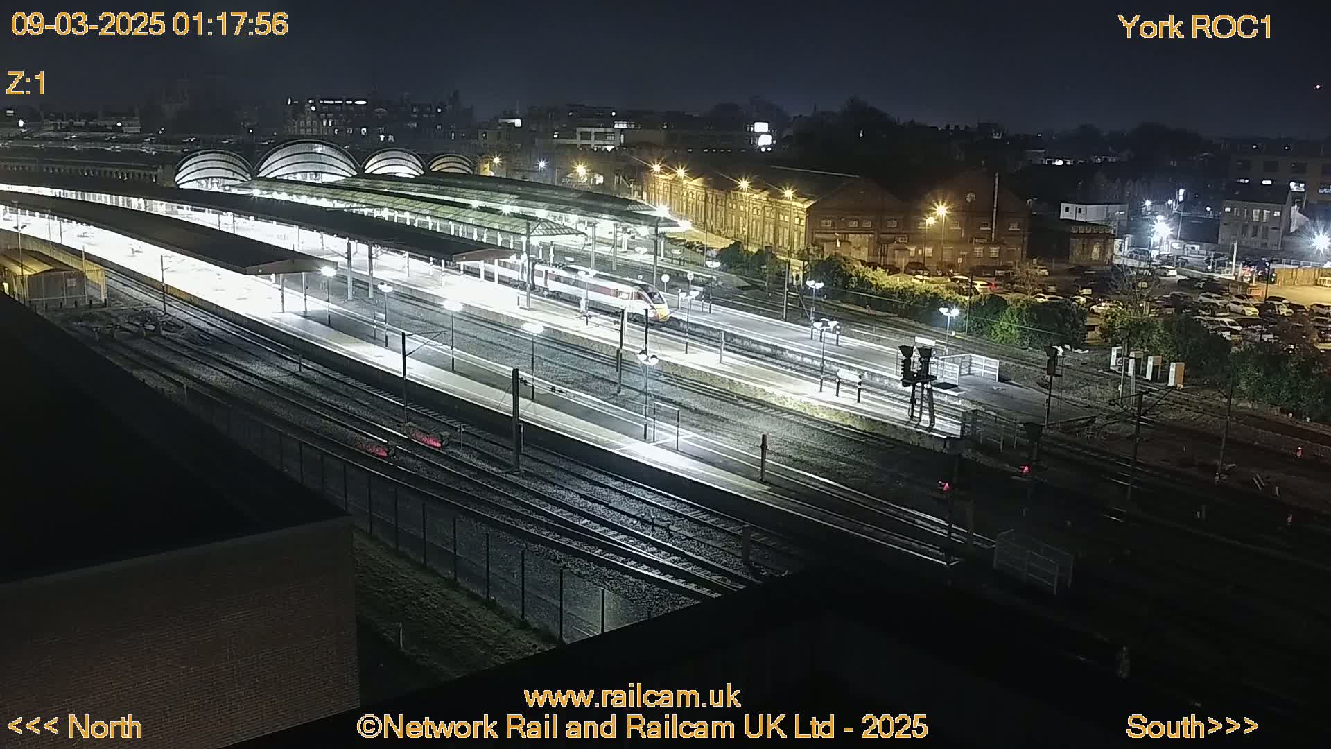 A high-angle nighttime view of a brightly lit train station with a train on the tracks.