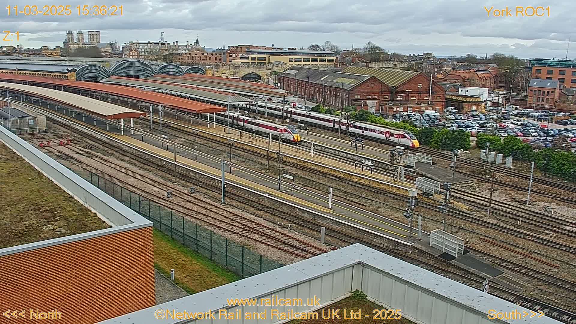 Two high-speed trains are at a railway station under an overcast sky.