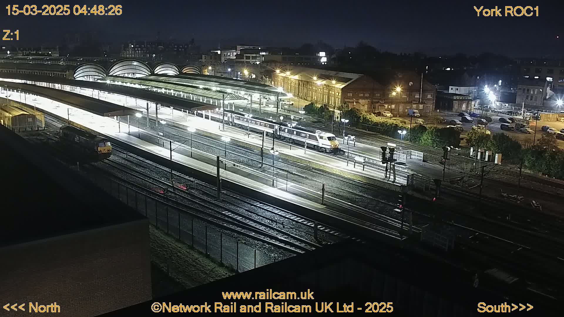 A nighttime aerial view of a train station with two trains and numerous tracks under bright lights.