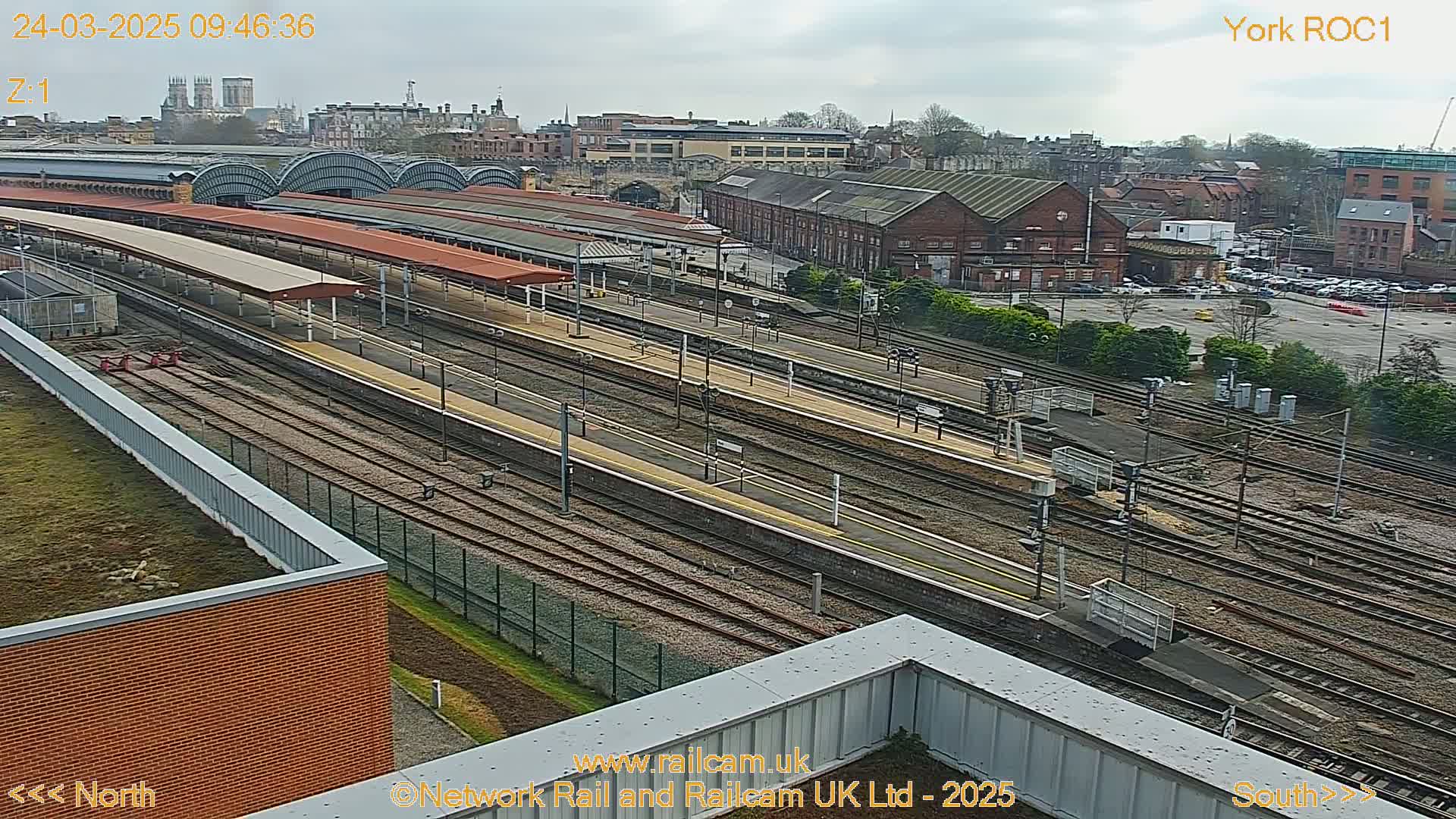 A high-angle view of a train station with numerous tracks and platforms under an overcast sky.