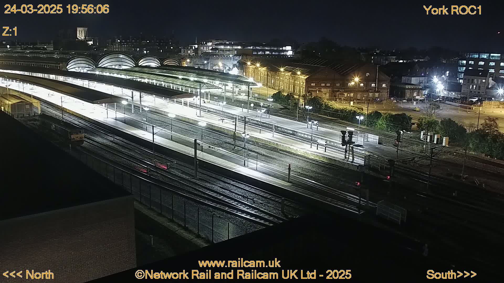 A nighttime, high-angle view of a brightly lit train station with numerous tracks and platforms.