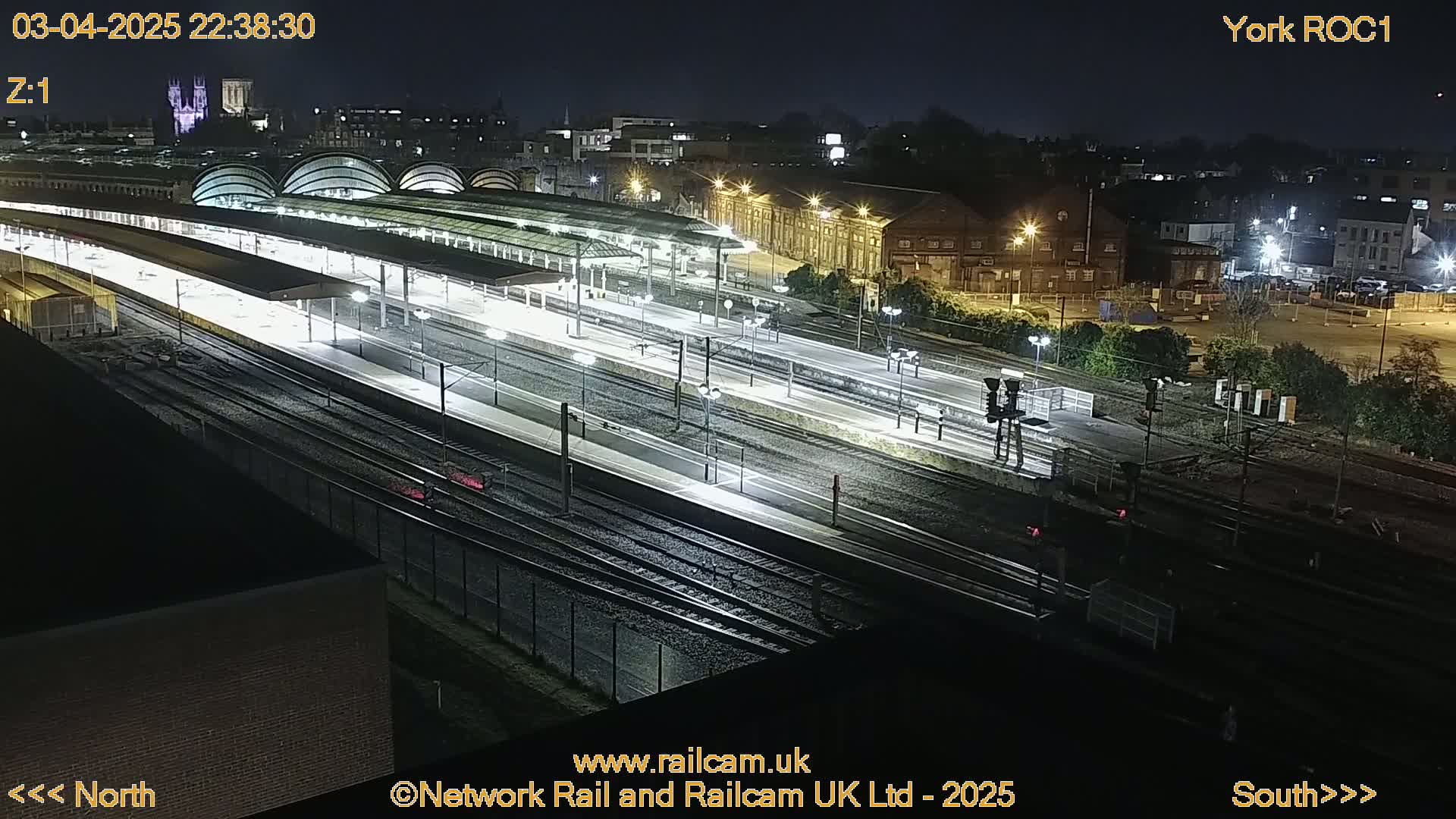 A nighttime, high-angle view of a brightly lit train station with numerous tracks and platforms.