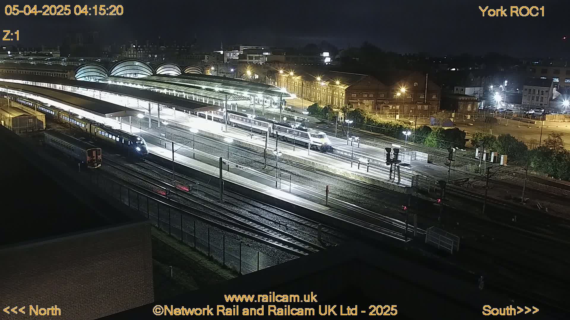 Several trains are at a brightly lit station at night.