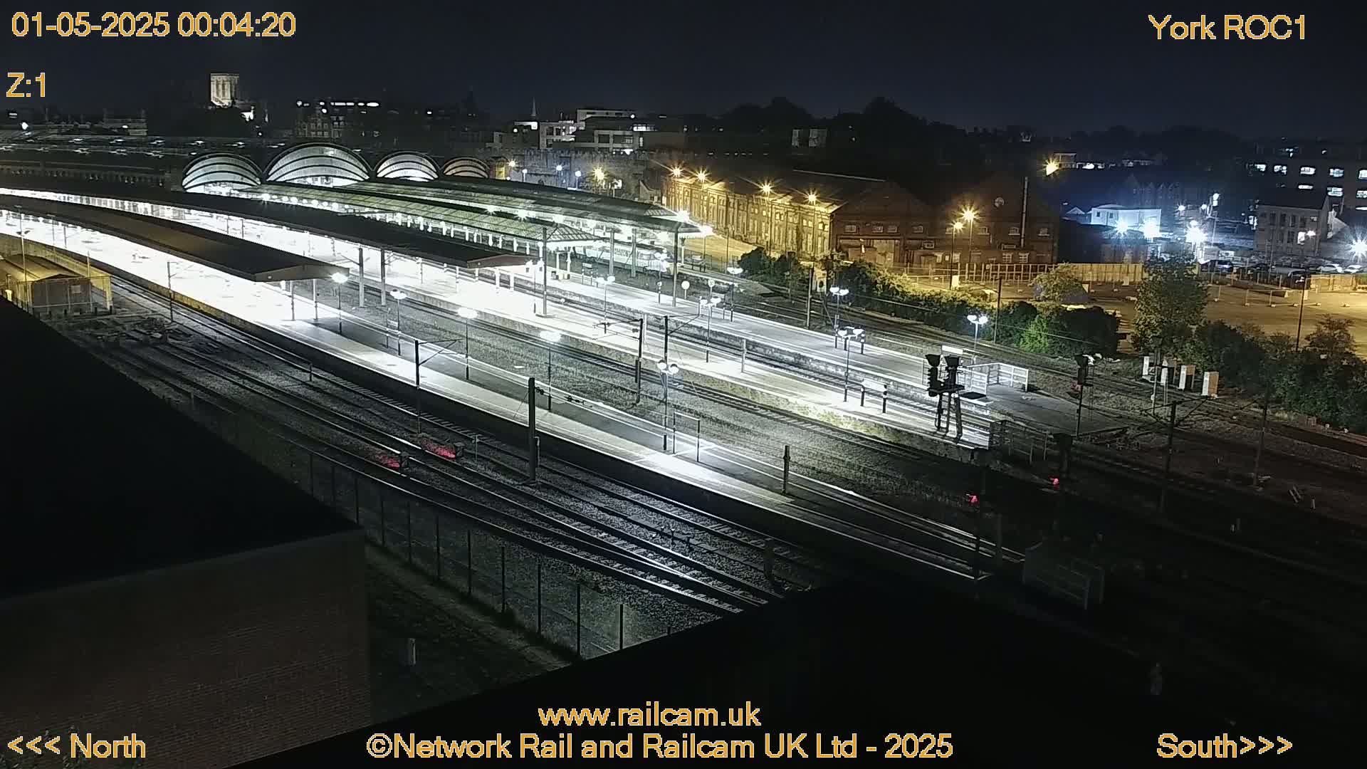 A nighttime aerial view of a brightly lit train station with many tracks and platforms.
